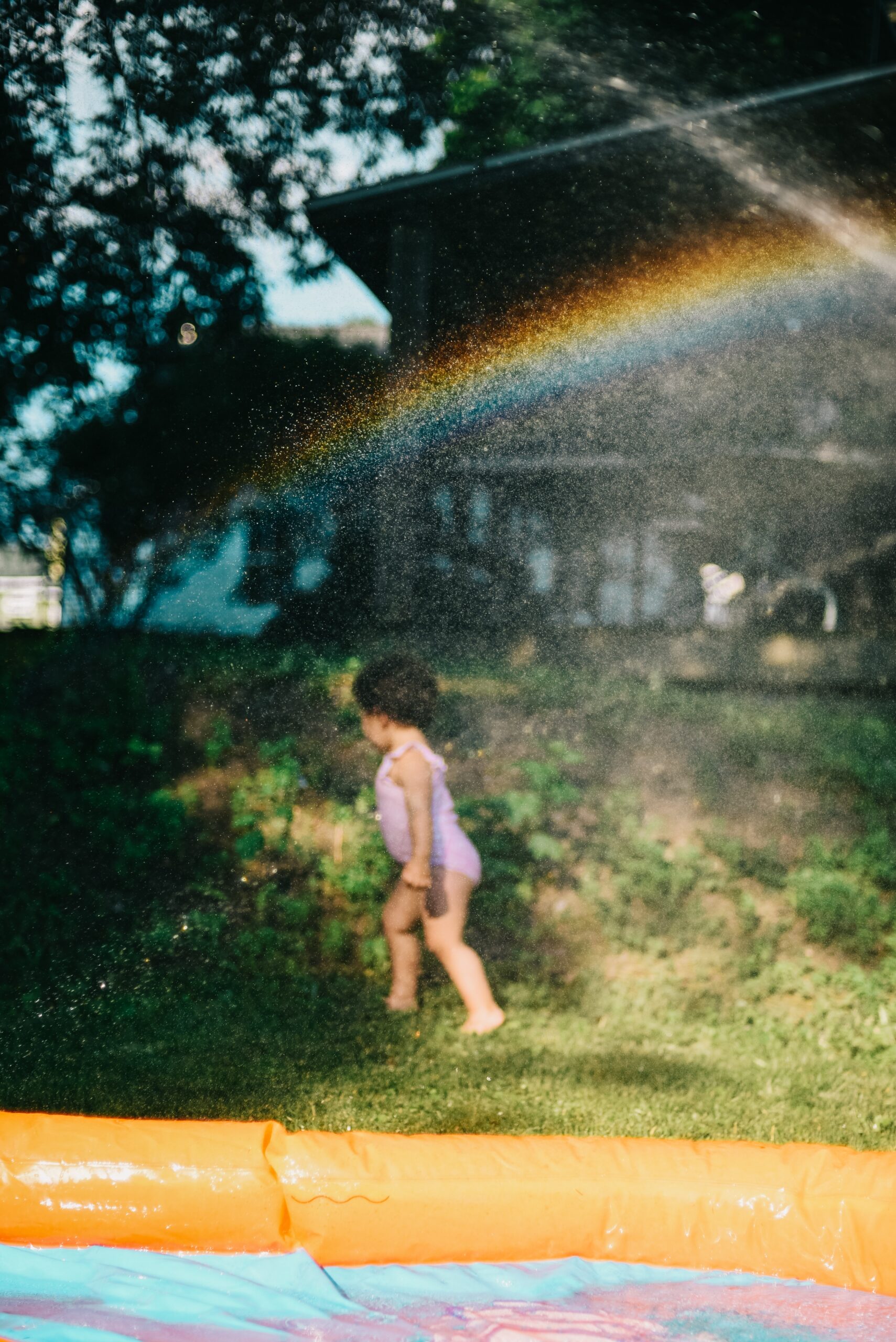 little girl running through the sprinkler under a rainbow, fully engulfed in the joy of movement and play