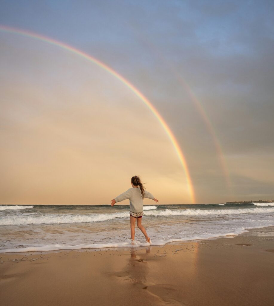 finding a moment of calm, inner child play, small girl running through a rainbow on the beach